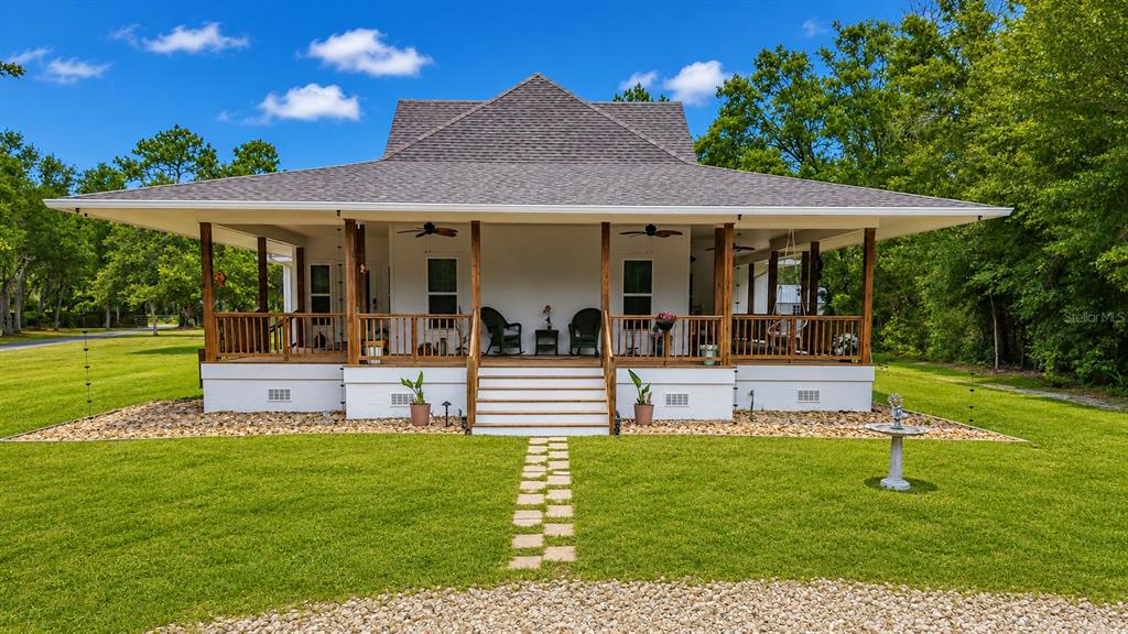 A white house with a large wraparound porch sits on a grassy lawn — 6687 W 7 RIVERS DRIVE, CRYSTAL RIVER, FL