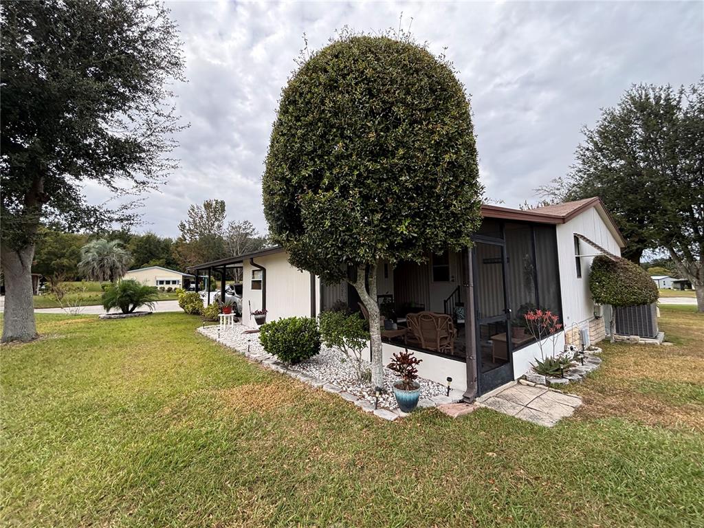 A side view of a manufactured home featuring a screened-in porch and landscaped yard — 3833 OLAX COURT, ZELLWOOD, FL