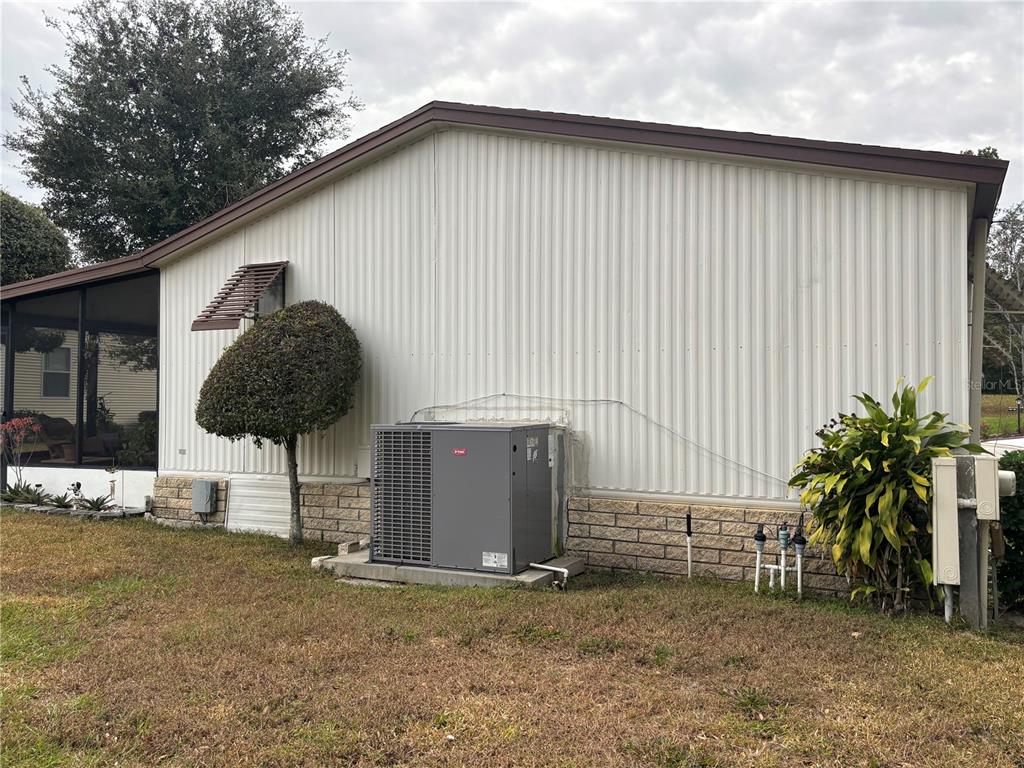 The exterior side of a manufactured home features a central HVAC unit and landscaping — 3833 OLAX COURT, ZELLWOOD, FL