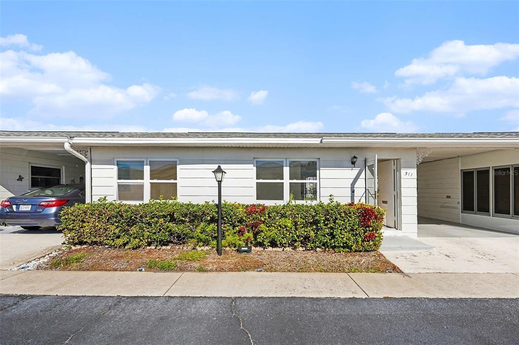 A single-story white house with a carport, a hedge, and a paved driveway — 12400 PARK BOULEVARD UNIT 311, SEMINOLE, FL