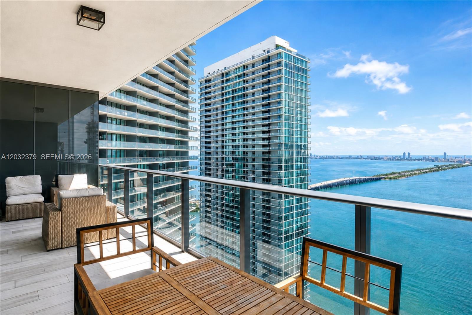 A balcony with outdoor furniture overlooks a bay, a bridge, and neighboring high-rise buildings — 480 NE 31st St # 3705, Miami FL 33137, MIAMI, FL