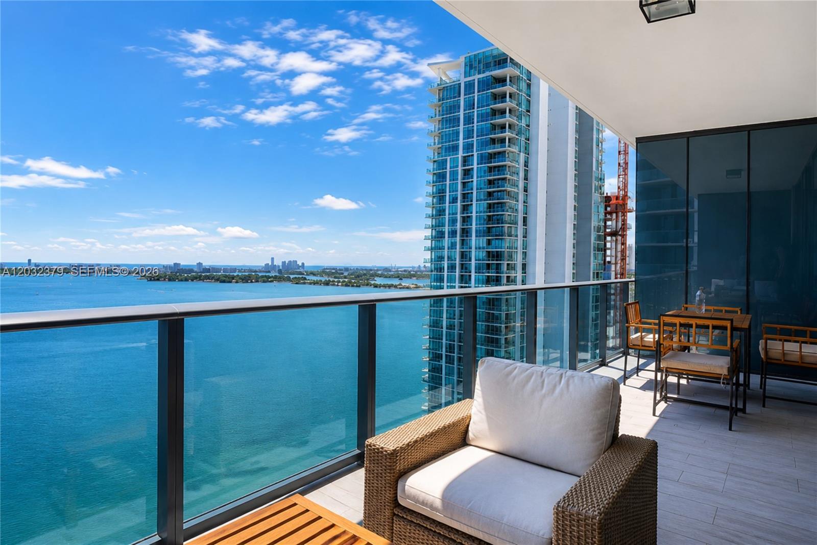 A balcony with outdoor furniture overlooks a bay and a neighboring high-rise building — 480 NE 31st St # 3705, Miami FL 33137, MIAMI, FL
