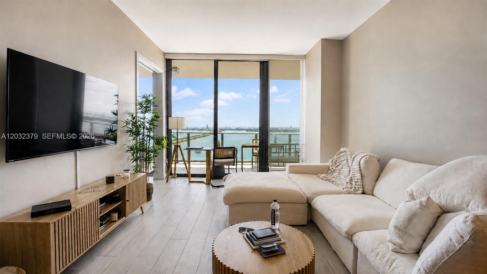 A living room features a sectional sofa, a wooden media console, and a balcony view — 480 NE 31st St # 3705, Miami FL 33137, MIAMI, FL