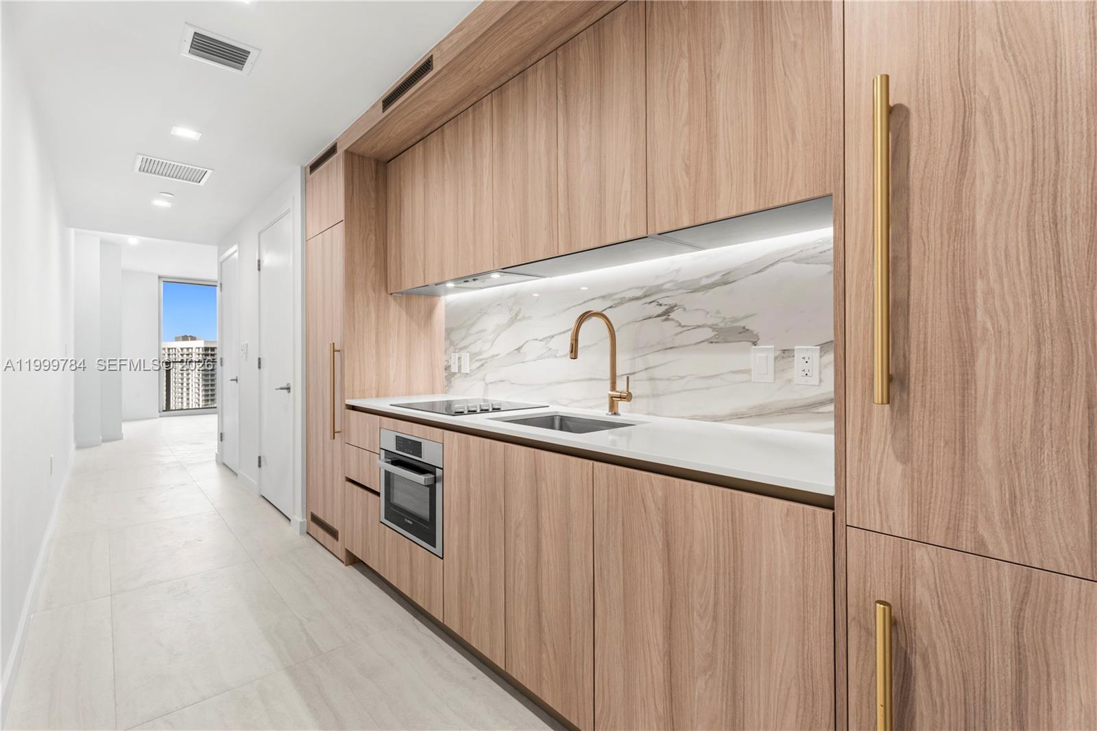 A modern kitchen features light wood cabinetry, a marble backsplash, and gold hardware — 77 SE 5th Street # 3304, Miami FL 33131, MIAMI, FL