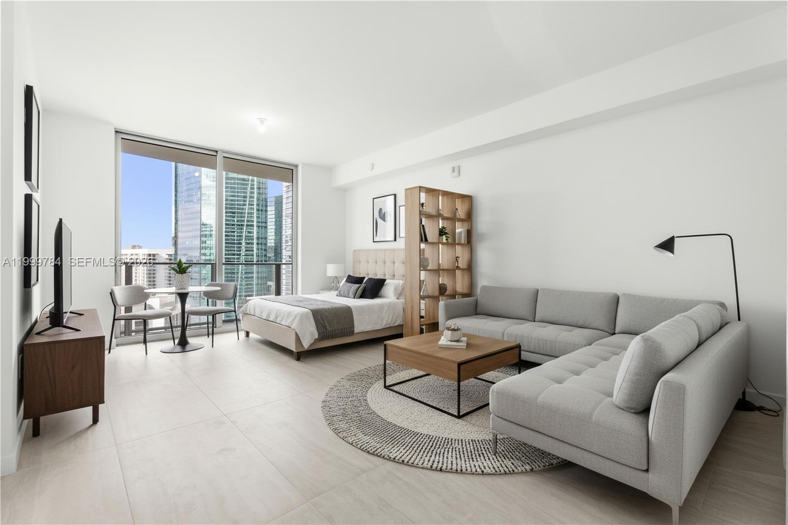 A modern studio apartment features a bed, sectional sofa, and floor-to-ceiling windows with city views — 77 SE 5th Street # 3304, Miami FL 33131, MIAMI, FL