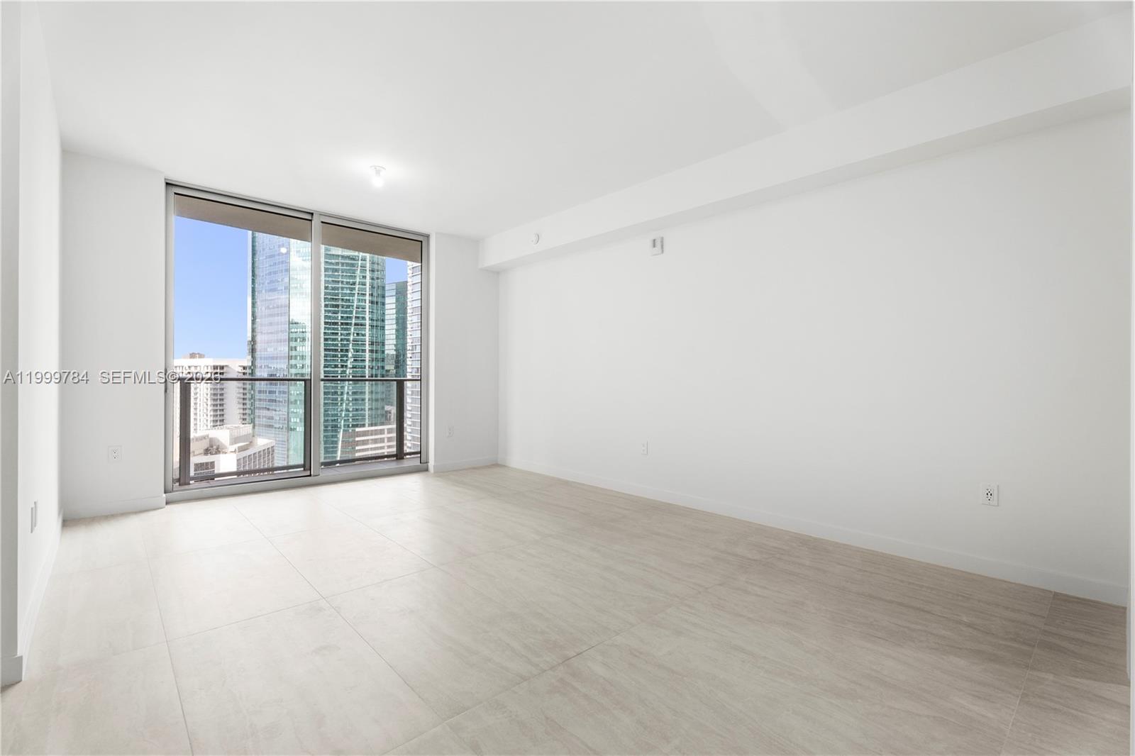 An empty room with light-colored tile flooring, white walls, and a large sliding glass door — 77 SE 5th Street # 3304, Miami FL 33131, MIAMI, FL