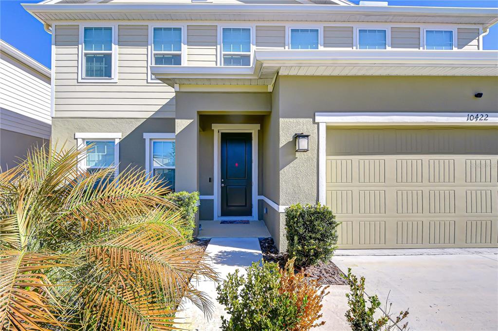 The exterior of a two-story house features a tan garage, a dark front door, and landscaping — 10422 GLIDING EAGLE WAY, LAND O LAKES, FL