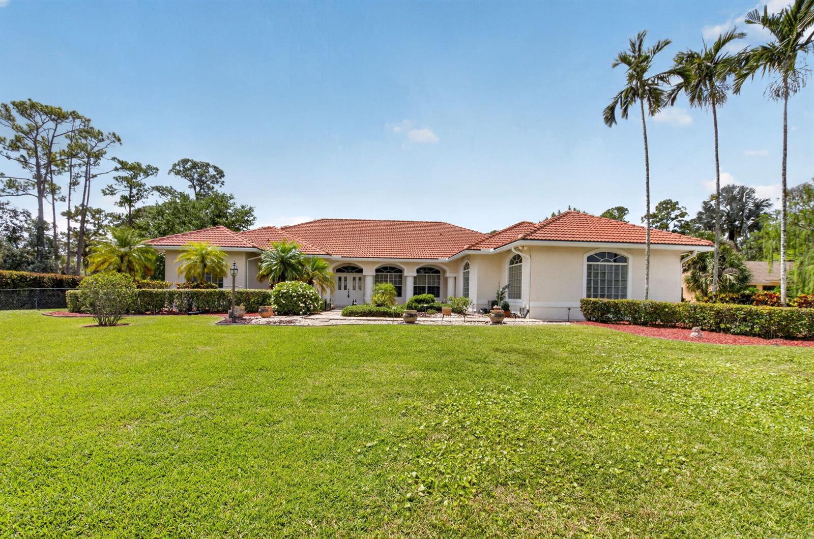 A single-story house with a terracotta tile roof and palm trees sits on a lawn — 9774 Saddle Court, Lake Worth FL 33467, LAKE WORTH, FL