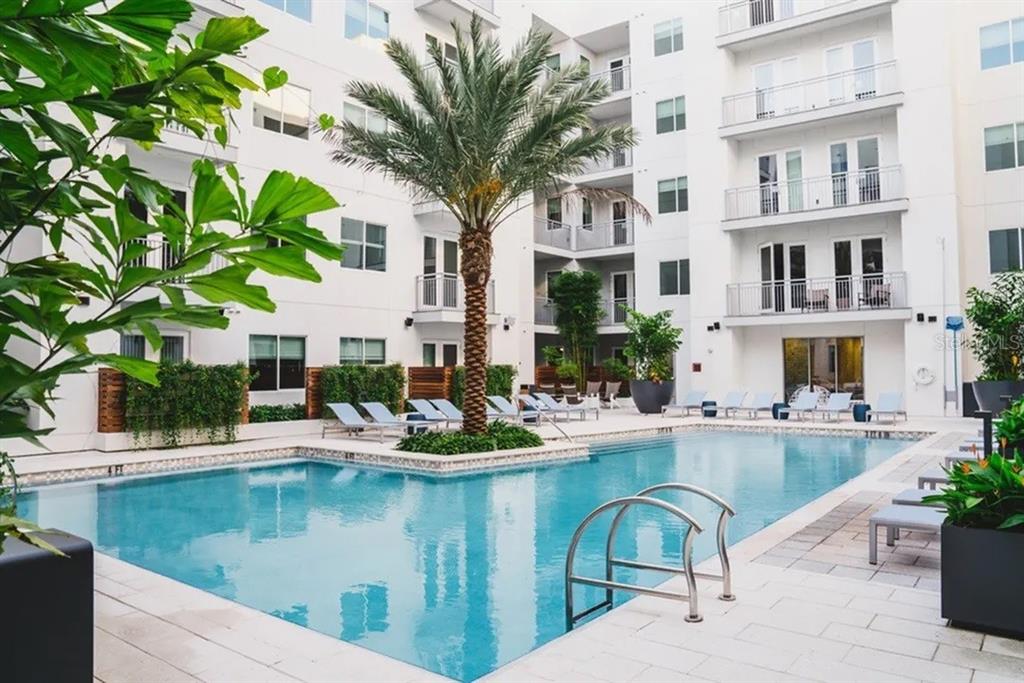 A swimming pool sits in the courtyard of a multi-story white apartment building with balconies — 505 CHATHAM AVENUE, ORLANDO, FL