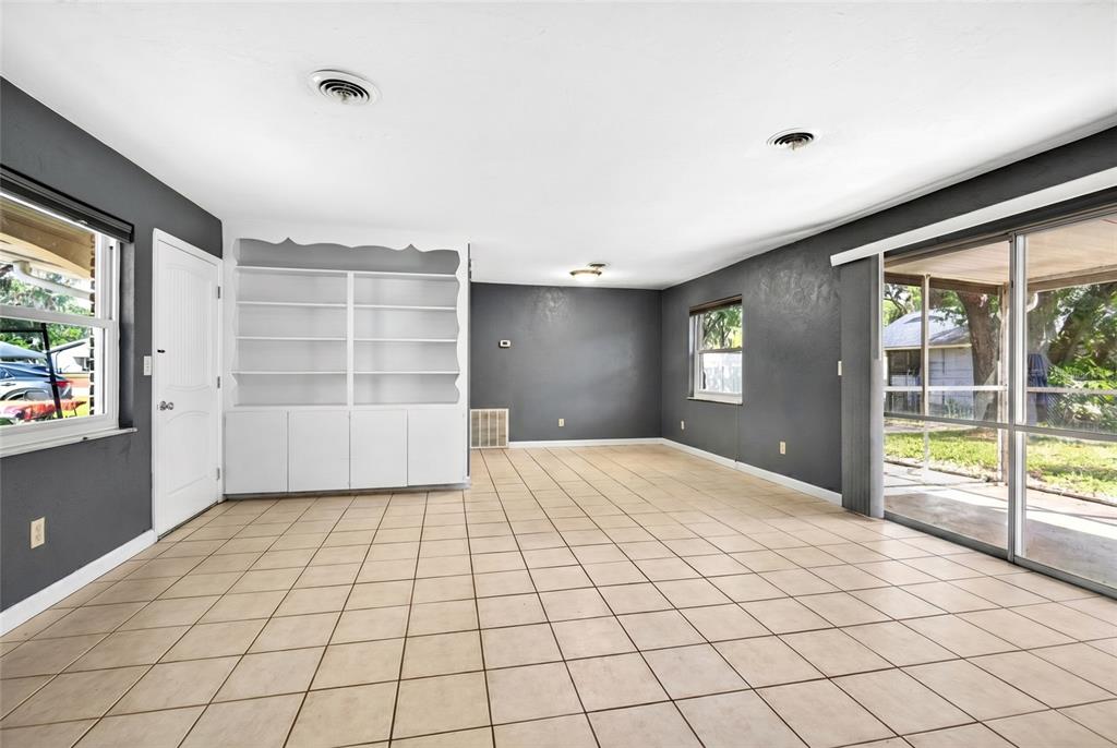 A living room with dark gray walls, white built-in shelving, tile flooring, and sliding glass doors — 2622 SW 35TH AVENUE, OCALA, FL