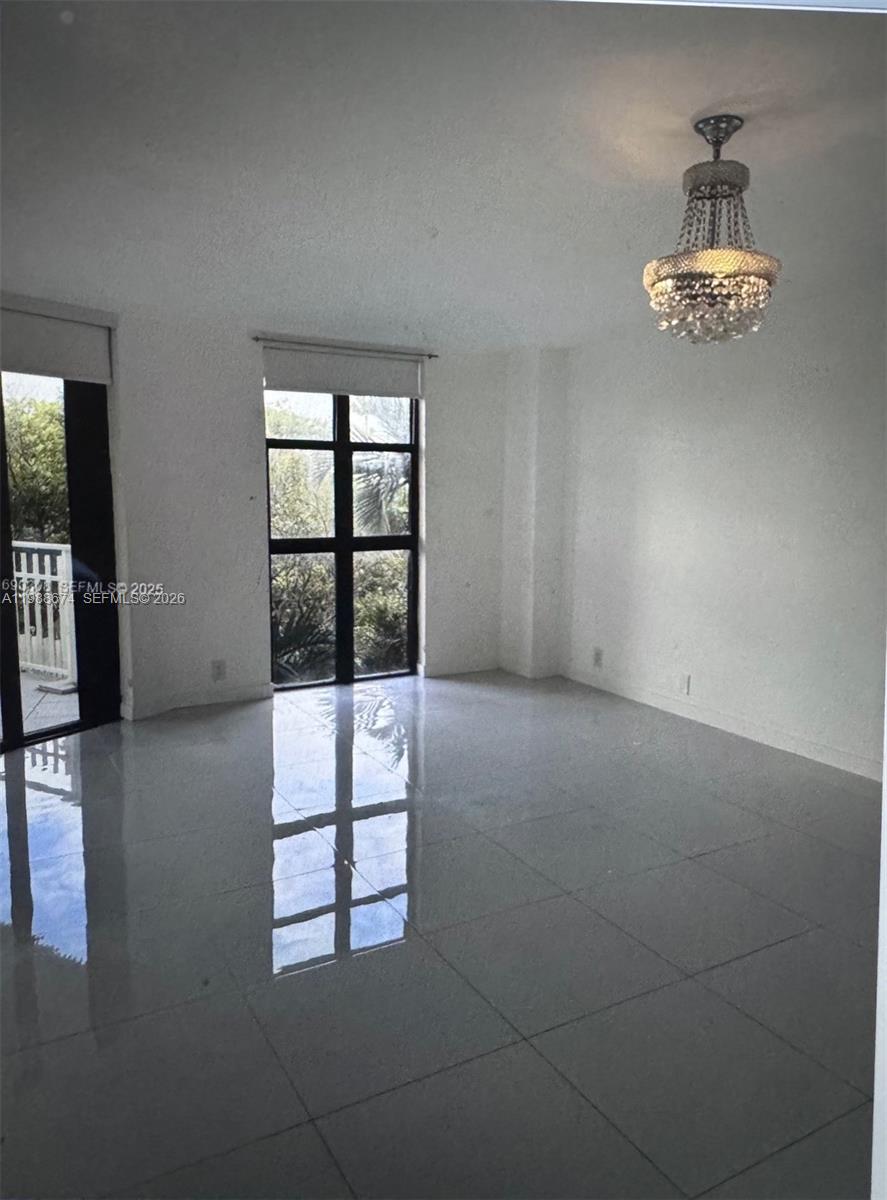 A bright, empty room features white walls, large windows, a crystal chandelier, and tiled floors — 4000 Towerside Ter # 609, Miami FL 33138, MIAMI, FL