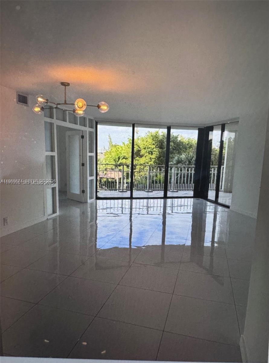 An empty room with white tile floors, a modern chandelier, and floor-to-ceiling glass balcony doors — 4000 Towerside Ter # 609, Miami FL 33138, MIAMI, FL