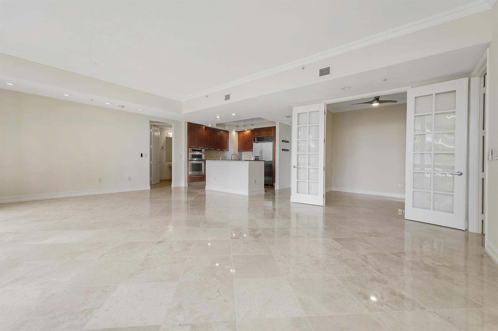 A spacious room with light-colored tile flooring, a kitchen with wood cabinets, and French doors — 701 S Olive Avenue # 1706, West Palm Beach FL 33401, WEST PALM BEACH, FL