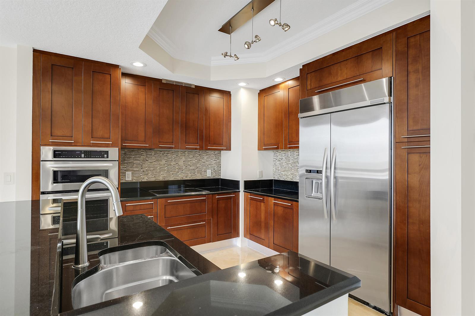 A kitchen features dark wood cabinets, black countertops, stainless steel appliances, and a double sink — 701 S Olive Avenue # 1706, West Palm Beach FL 33401, WEST PALM BEACH, FL