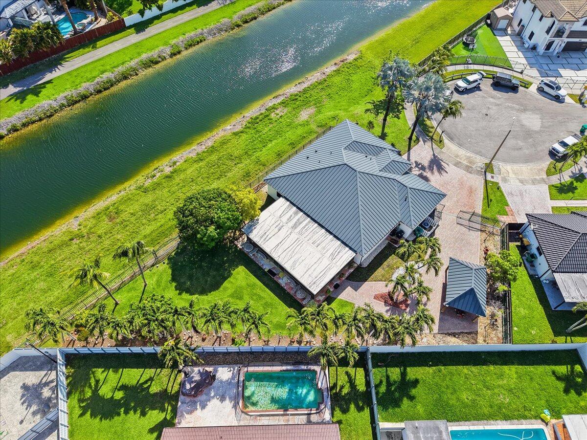 An aerial view shows a house with a metal roof, patio, and pool by a canal — 20300 SW 129th Place, Miami FL 33177, MIAMI, FL