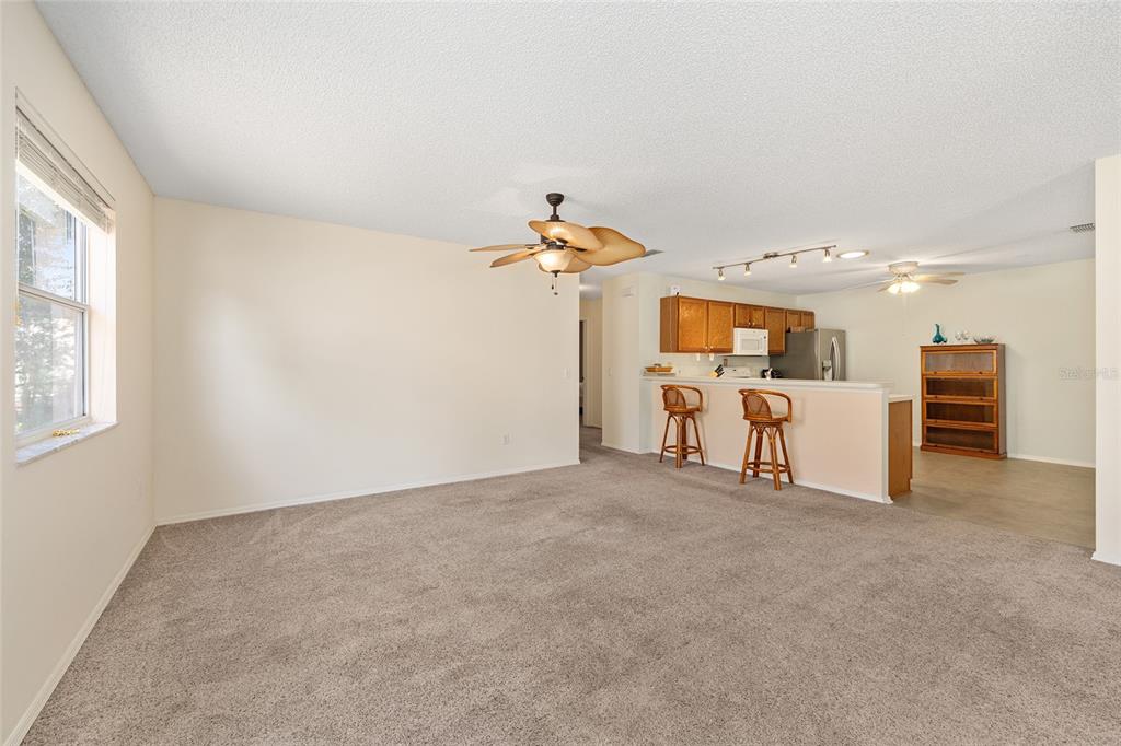 A carpeted living room opens to a kitchen with a breakfast bar and wooden cabinets — 1710 ROSALES ROAD, THE VILLAGES, FL
