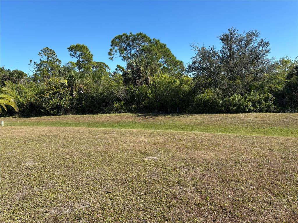 A grassy lot features a gentle slope leading to a dense line of trees — 7466 SILAGE CIR, PORT CHARLOTTE, FL