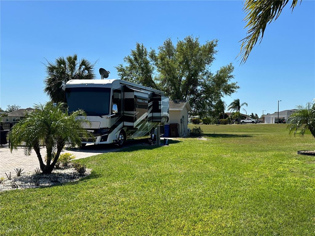 A large recreational vehicle is parked on a paved driveway next to a grassy lawn — 728 TEABERRY TRAIL, POLK CITY, FL