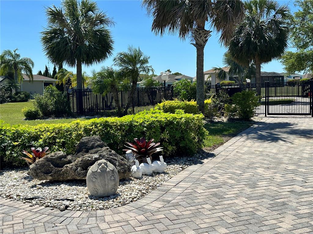 A paved driveway leads to a landscaped garden bed featuring a stone sculpture and palm trees — 728 TEABERRY TRAIL, POLK CITY, FL