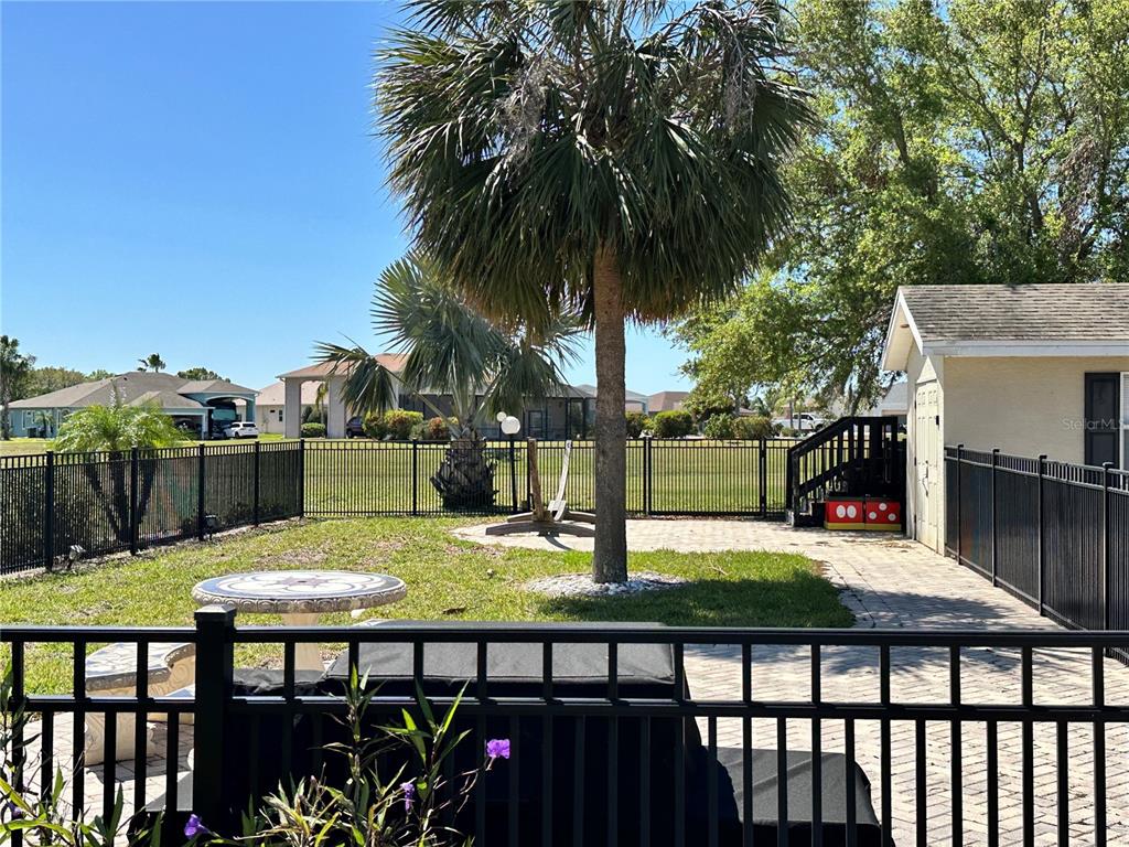A fenced backyard features a palm tree, a paved patio, and a small play structure — 728 TEABERRY TRAIL, POLK CITY, FL