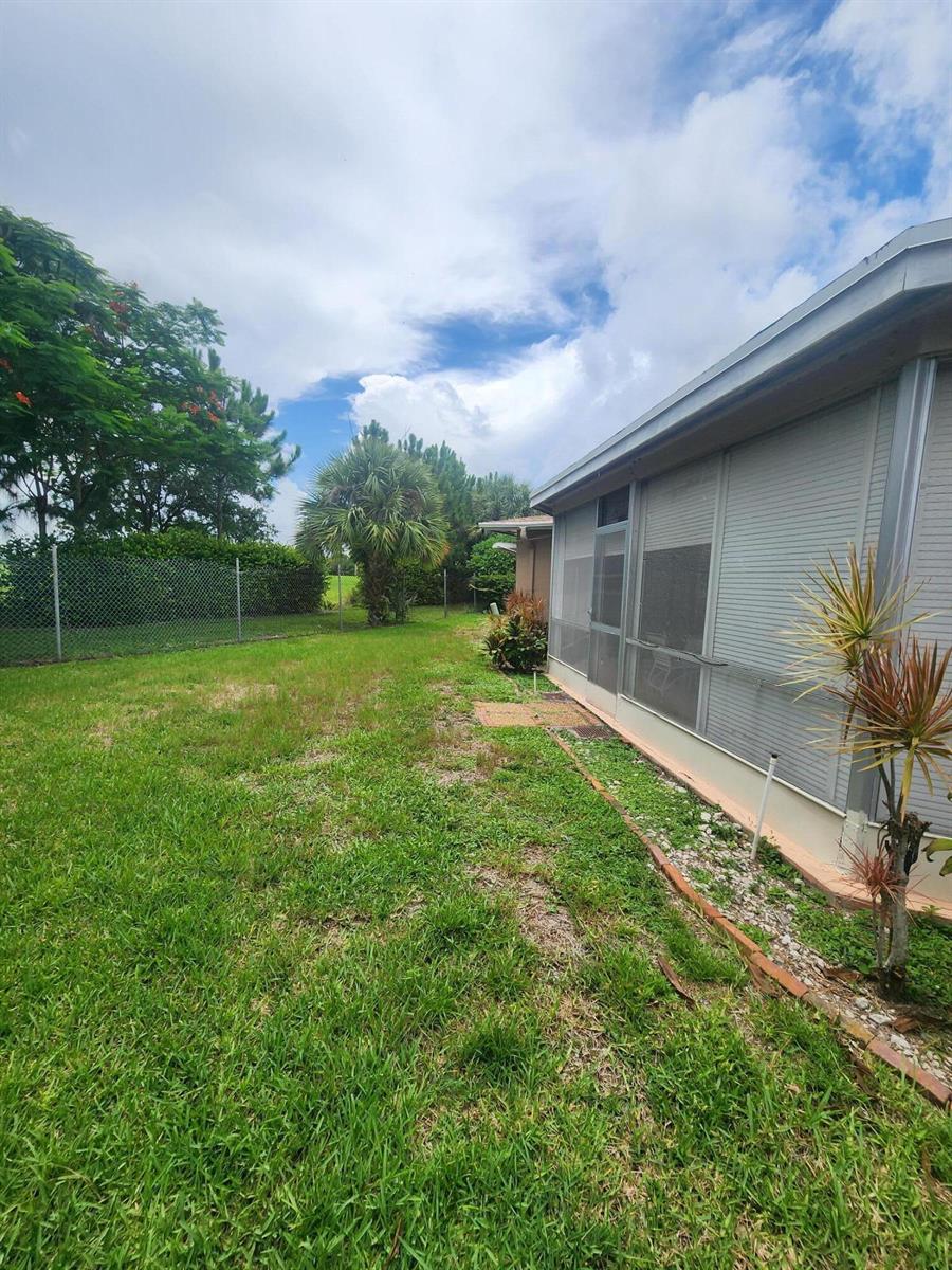 A grassy backyard features a chain-link fence, a palm tree, and a screened-in patio area — 4821 NW 13th Avenue, Deerfield Beach FL 33064, DEERFIELD BEACH, FL