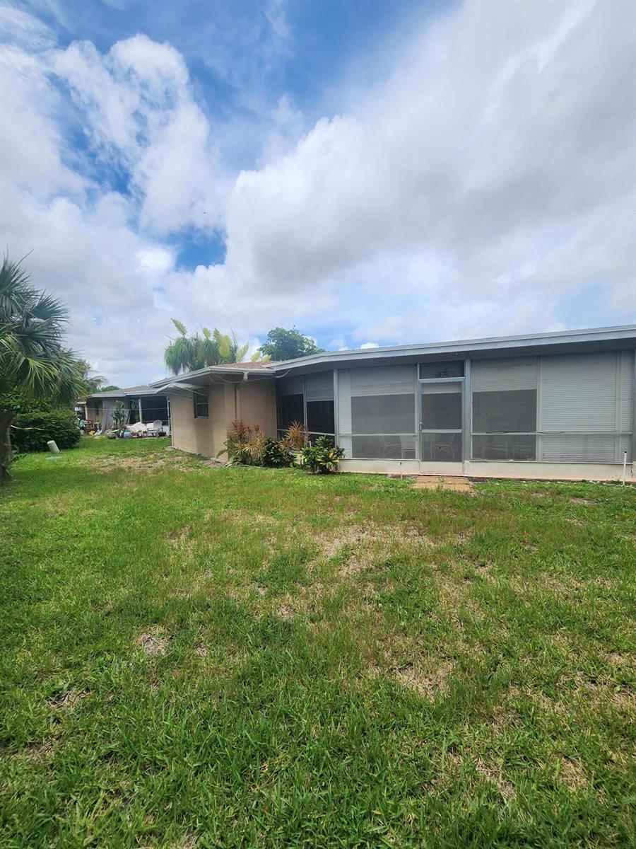 The exterior of a single-story house features a screened-in porch and a grassy backyard — 4821 NW 13th Avenue, Deerfield Beach FL 33064, DEERFIELD BEACH, FL