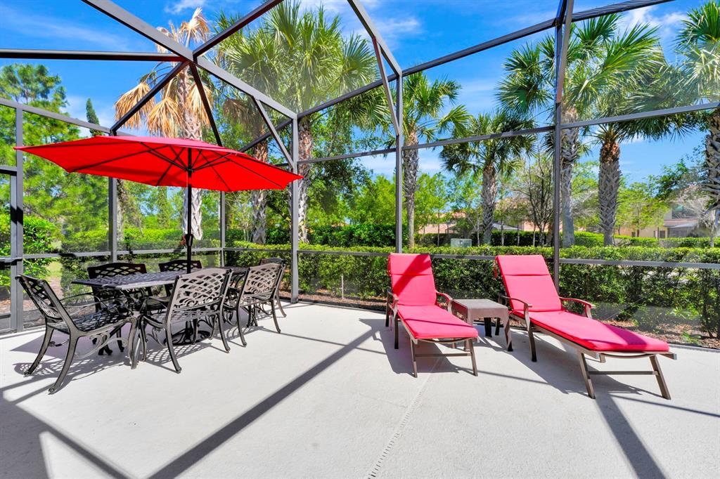 A screened-in patio features a dining set with a red umbrella and two lounge chairs — 4416 ACORN COURT, DAVENPORT, FL