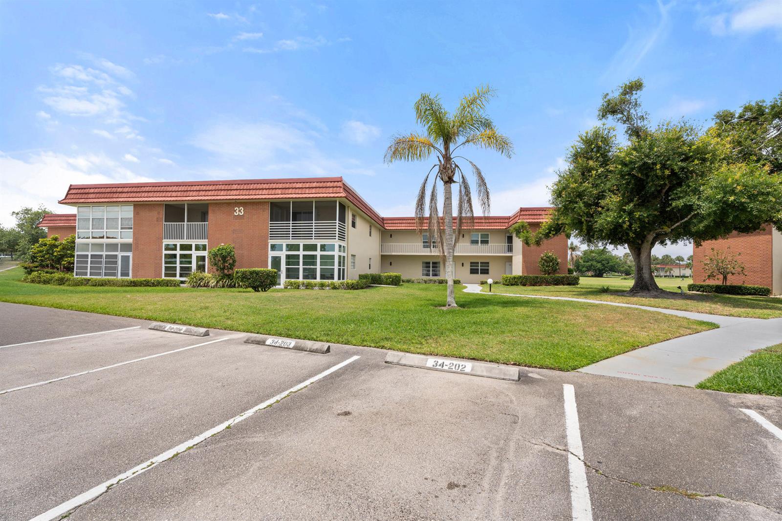 A two-story brick apartment building with a palm tree and parking spaces in front — 33 Pine Arbor Lane # 102, Vero Beach FL 32962, VERO BEACH, FL