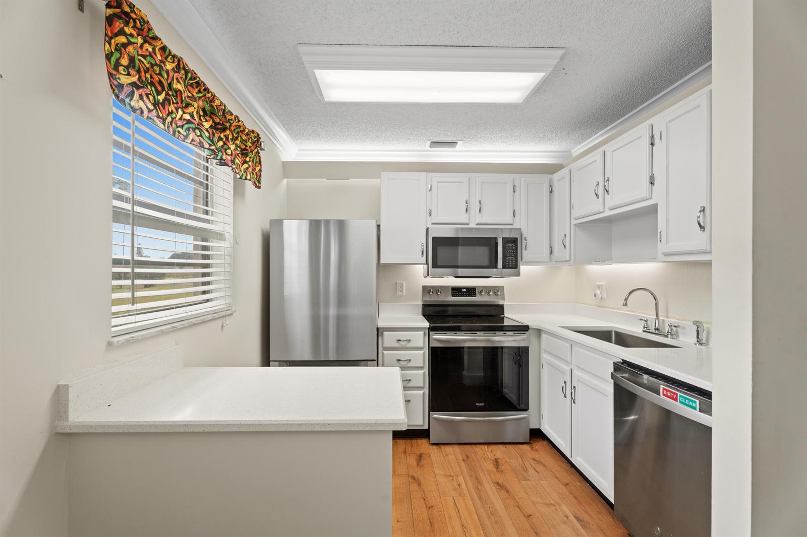 A kitchen features white cabinets, stainless steel appliances, a peninsula, and wood-look flooring — 33 Pine Arbor Lane # 102, Vero Beach FL 32962, VERO BEACH, FL