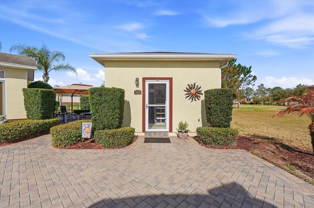 A light-colored house exterior features a paved walkway, manicured hedges, and a glass storm door — 326 NOLANE LANE, POLK CITY, FL