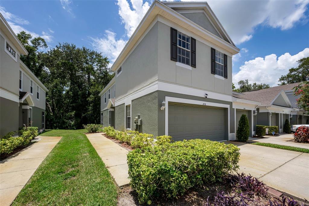 A two-story townhouse exterior features a gray garage, beige siding, and a landscaped front yard — 2418 EARLSWOOD COURT, BRANDON, FL
