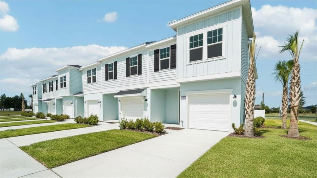A row of light blue two-story townhomes with white garage doors and green lawns — 6844 HOLCOMBE DOWN DRIVE, ZEPHYRHILLS, FL