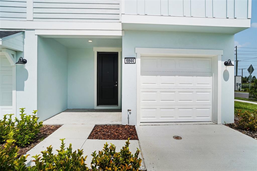 A light blue two-story townhouse exterior features a black front door and a white garage — 6844 HOLCOMBE DOWN DRIVE, ZEPHYRHILLS, FL