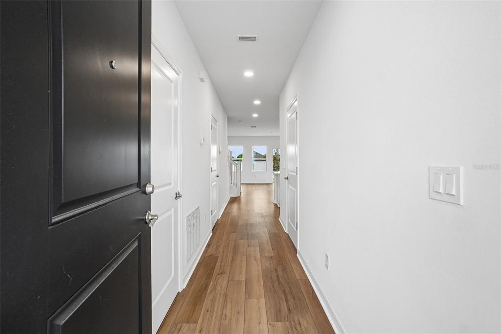 A hallway with wood-look flooring leads toward a bright living area with a staircase — 6844 HOLCOMBE DOWN DRIVE, ZEPHYRHILLS, FL