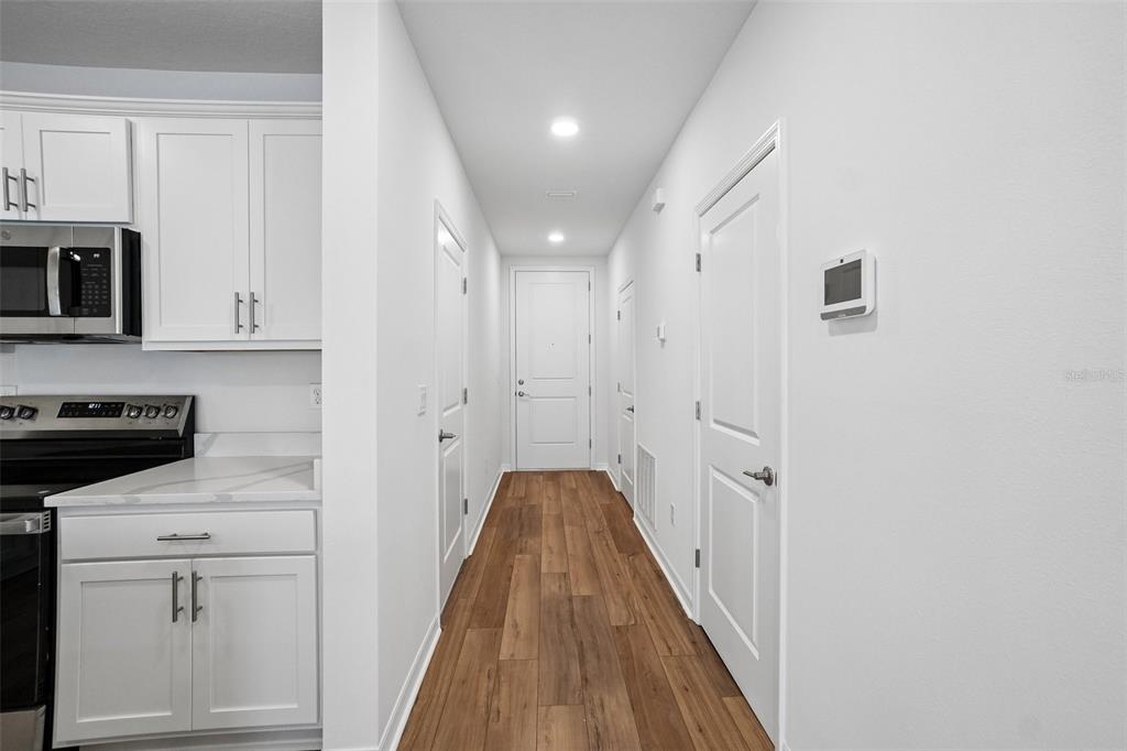 A hallway with wood-look flooring leads to a white door, flanked by white cabinetry — 6844 HOLCOMBE DOWN DRIVE, ZEPHYRHILLS, FL