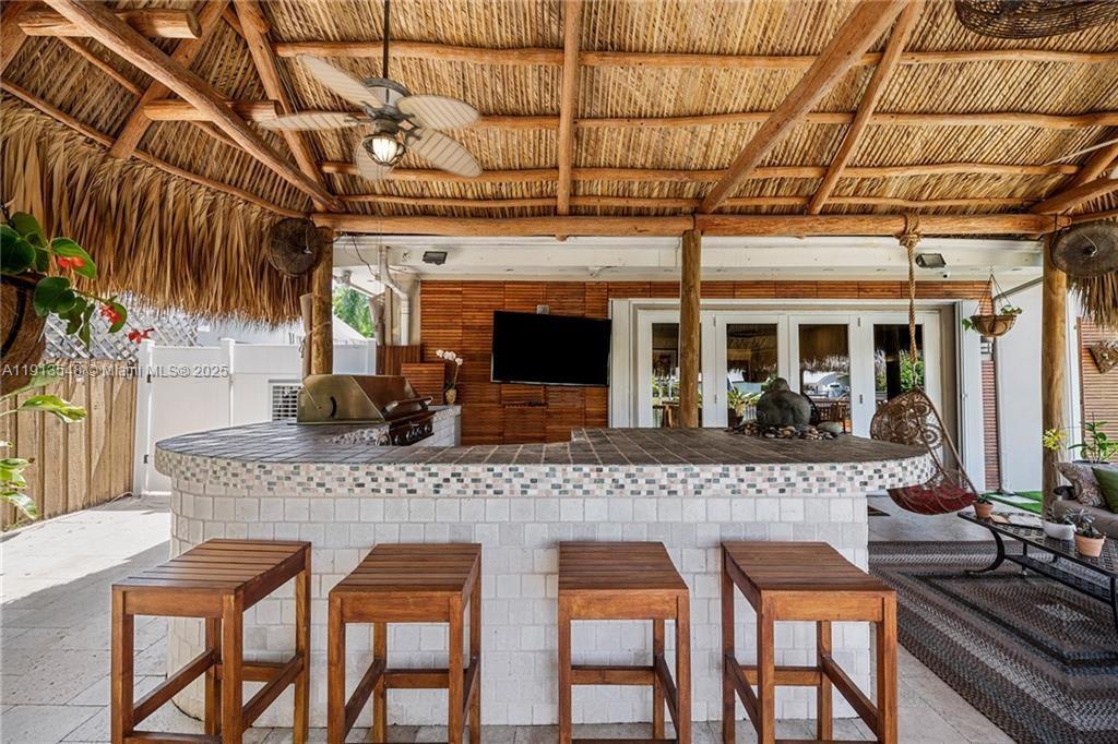 A covered outdoor patio features a tiled bar with four wooden stools and a grill — 21280 NE 23rd Ave, Miami FL 33180, MIAMI, FL