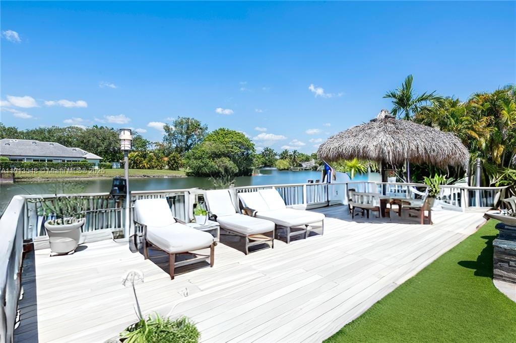 A wooden deck features lounge chairs and a tiki hut overlooking a calm canal — 21280 NE 23rd Ave, Miami FL 33180, MIAMI, FL