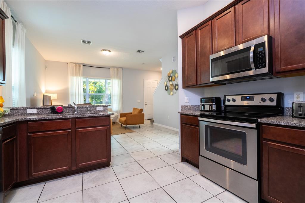 A kitchen with dark wood cabinets and stainless steel appliances overlooks an open living area — 9231 GRAND ISLAND WAY, WINTER GARDEN, FL