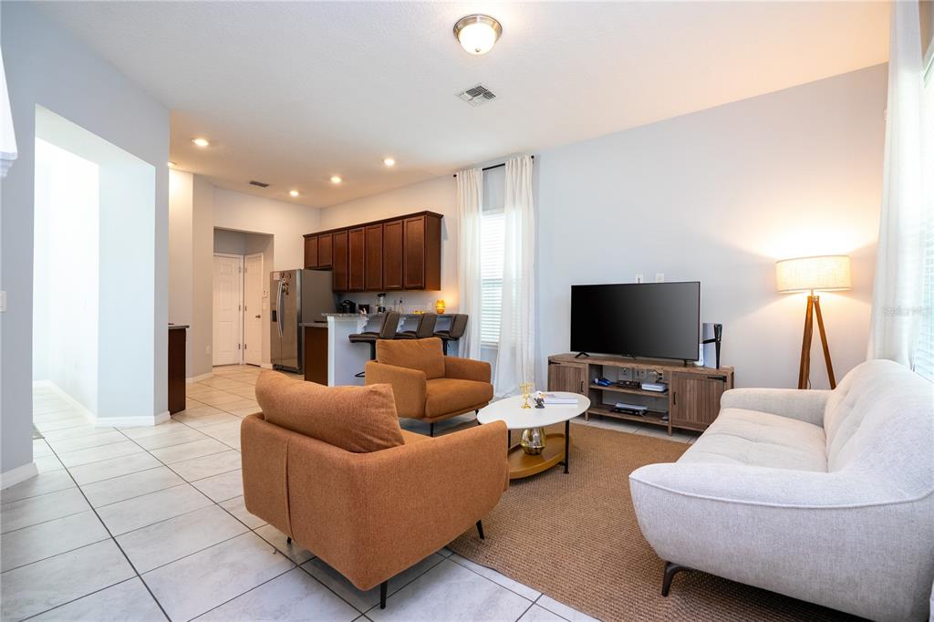 A living room with two orange armchairs, a white sofa, and an open kitchen area — 9231 GRAND ISLAND WAY, WINTER GARDEN, FL
