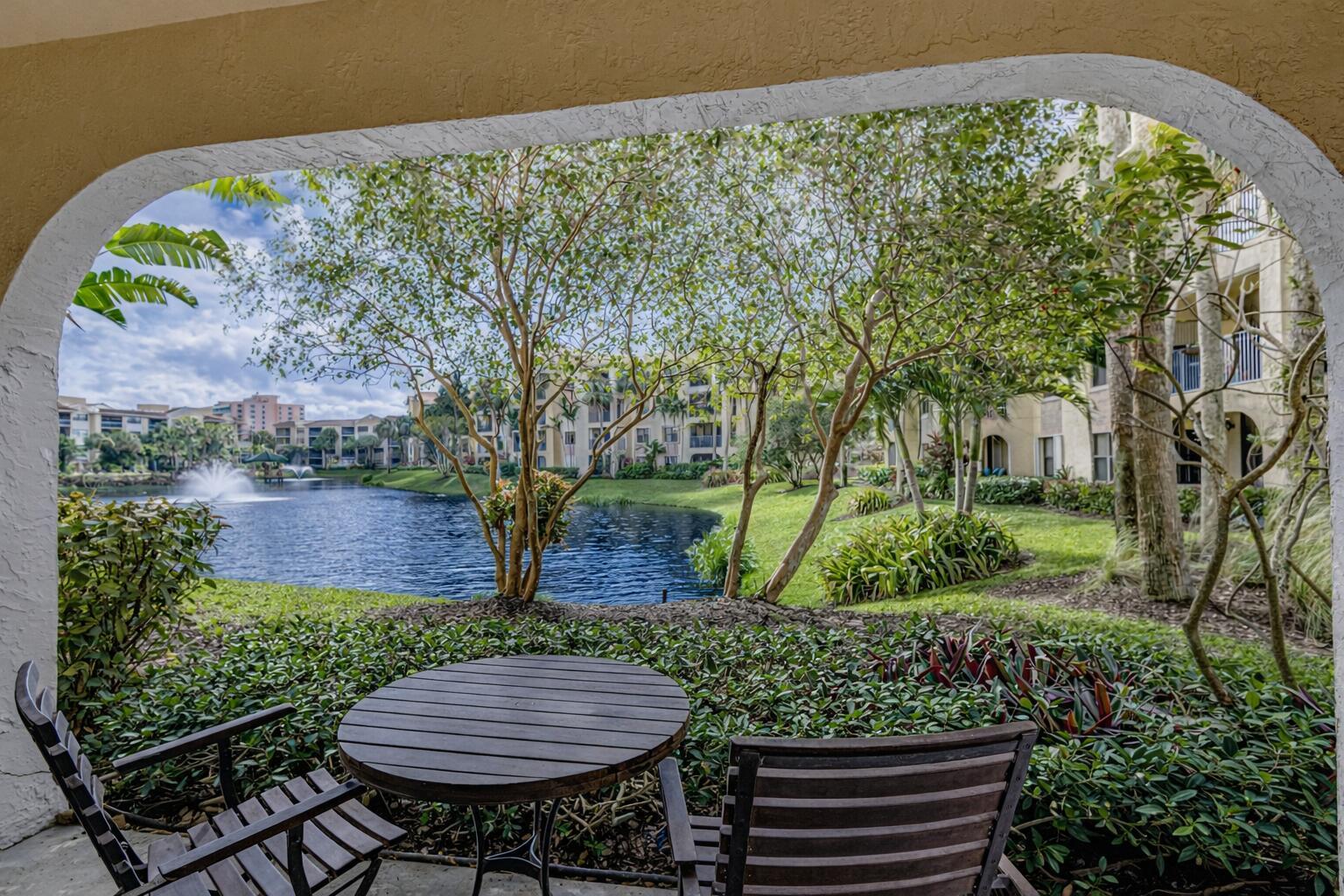 A patio with a table and chairs overlooks a pond and apartment buildings — 200 Uno Lago Drive # 105, Juno Beach FL 33408, JUNO BEACH, FL