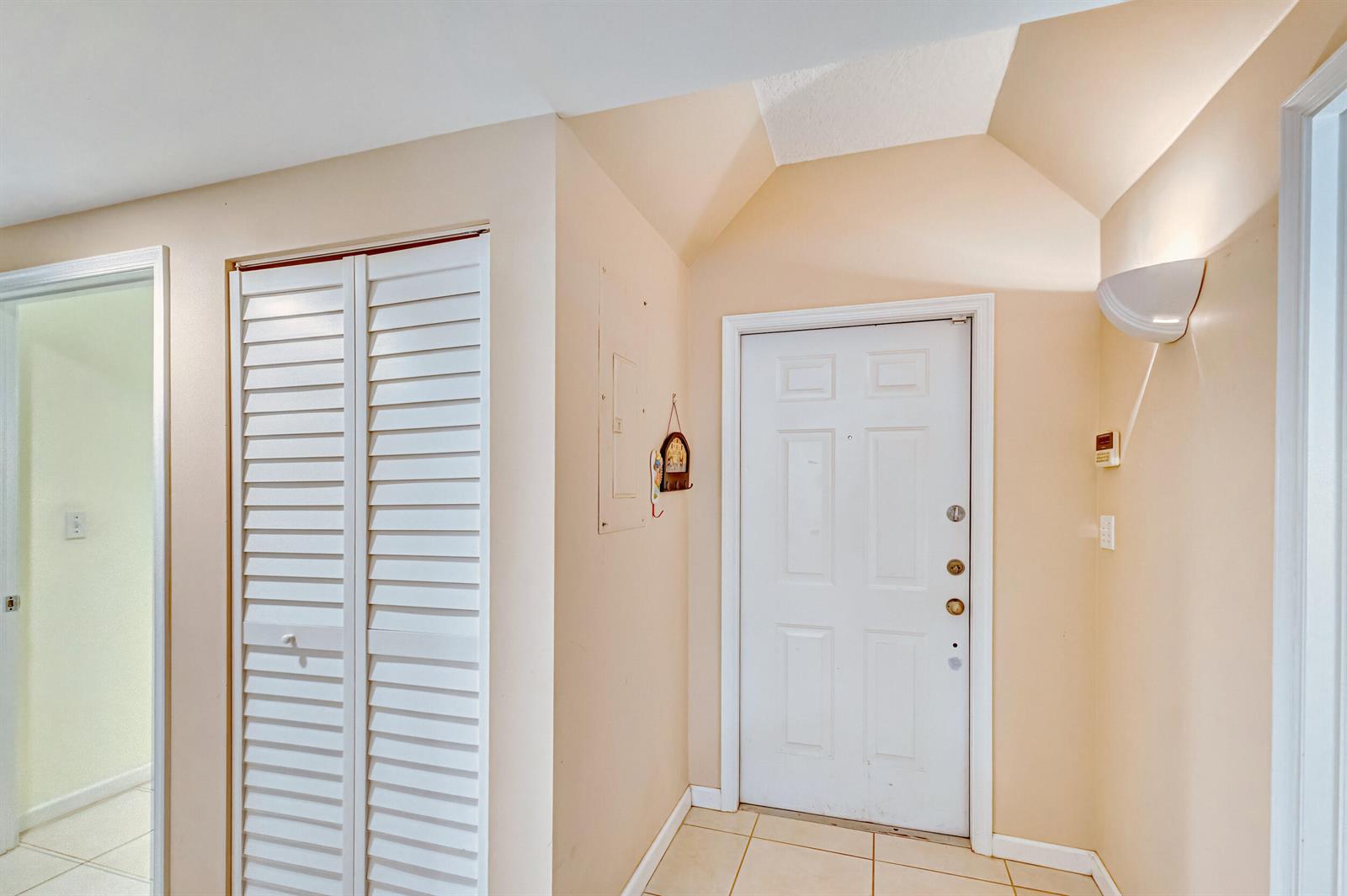 An entryway features a white front door, a louvered closet, and beige walls — 200 Uno Lago Drive # 105, Juno Beach FL 33408, JUNO BEACH, FL