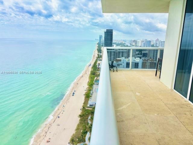 A high-rise balcony overlooks a sandy beach and the ocean with city buildings in distance — 1830 S Ocean Dr # 3702, Hallandale Beach FL 33009, HALLANDALE BEACH, FL