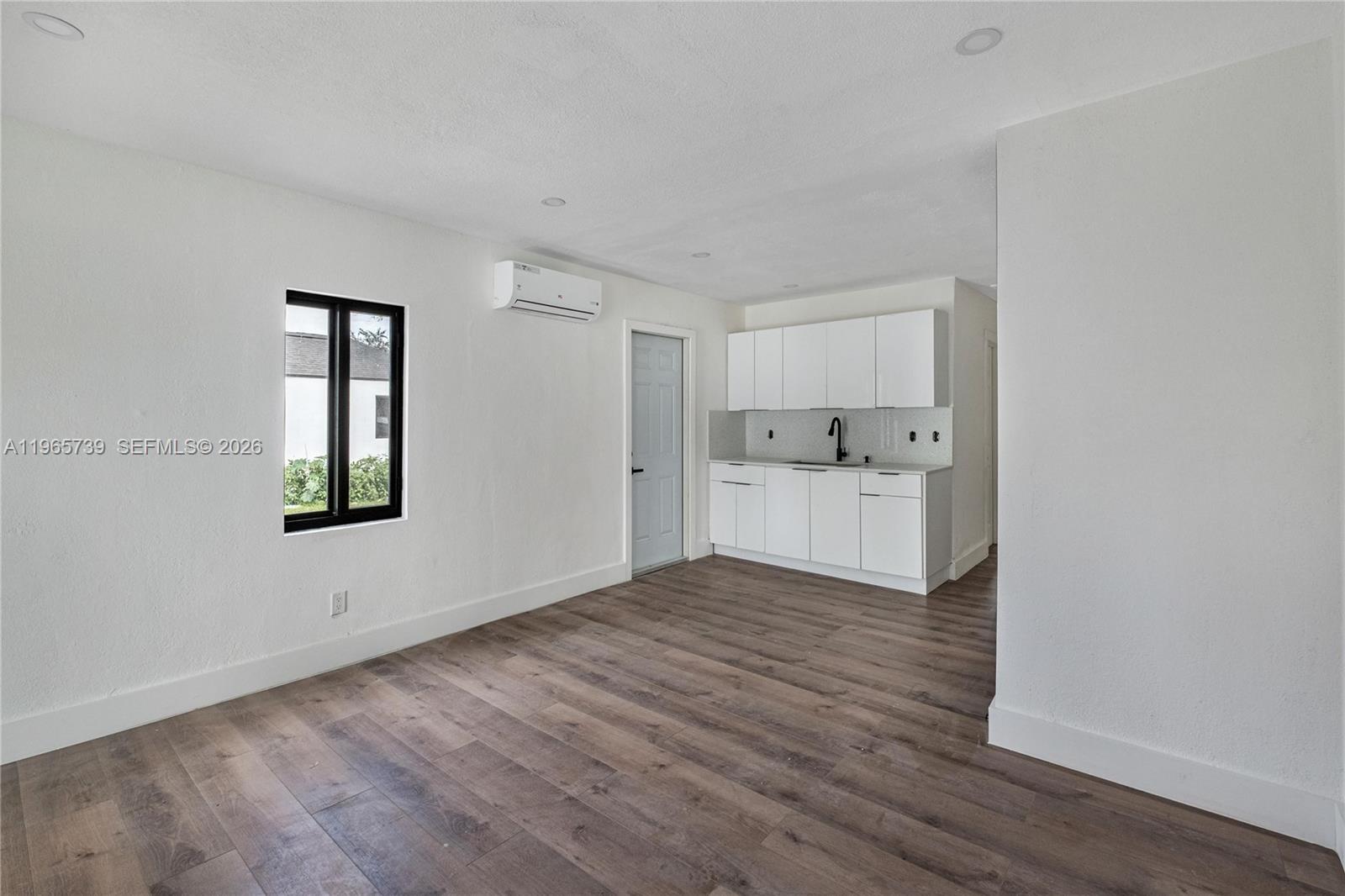 This room features white walls, wood-look flooring, a small kitchenette, and a wall-mounted air conditioner — 6905 NW 4th Ct # B, Miami FL 33150, MIAMI, FL