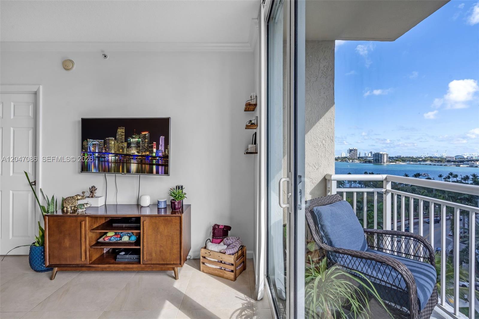 A living room with a wooden media console, wall-mounted television, and a balcony overlooking water — 2000 N Bayshore Dr # 909, Miami FL 33137, MIAMI, FL