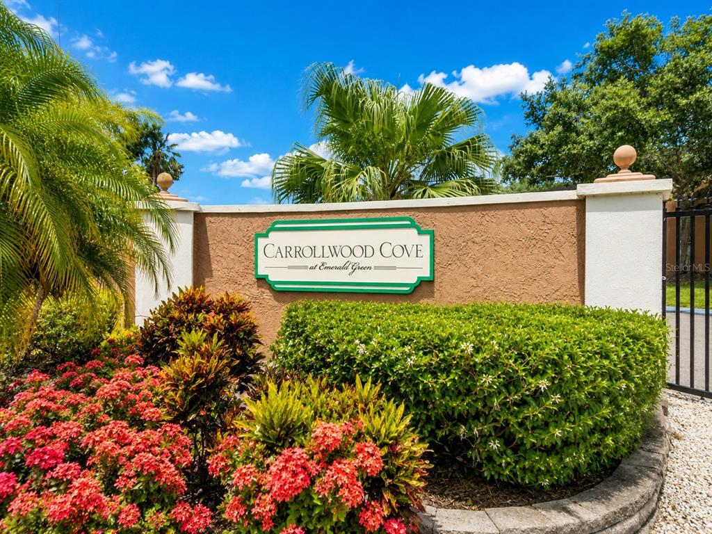 A sign for Carrollwood Cove at Emerald Green stands before a stucco wall and landscaping — 14623 PAR CLUB CIRCLE UNIT 14623, TAMPA, FL