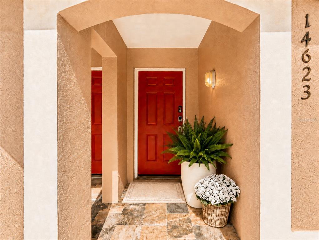 A red front door is framed by a tan stucco archway with a potted fern — 14623 PAR CLUB CIRCLE UNIT 14623, TAMPA, FL