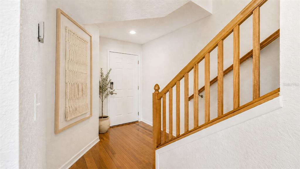 An entryway features hardwood floors, a white front door, and a wooden staircase railing — 14623 PAR CLUB CIRCLE UNIT 14623, TAMPA, FL