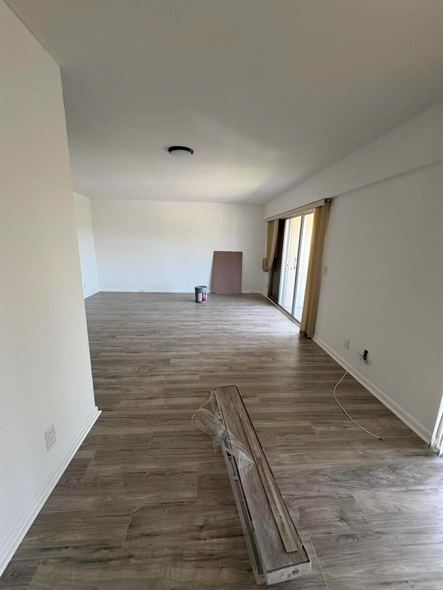 An empty room features light wood-look flooring, white walls, and a sliding glass door — 497 Mansfield L, Boca Raton FL 33434, BOCA RATON, FL