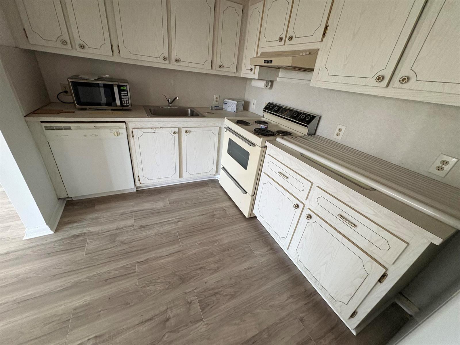 A kitchen features white cabinets, light wood-look flooring, a stove, a dishwasher, and a sink — 497 Mansfield L, Boca Raton FL 33434, BOCA RATON, FL