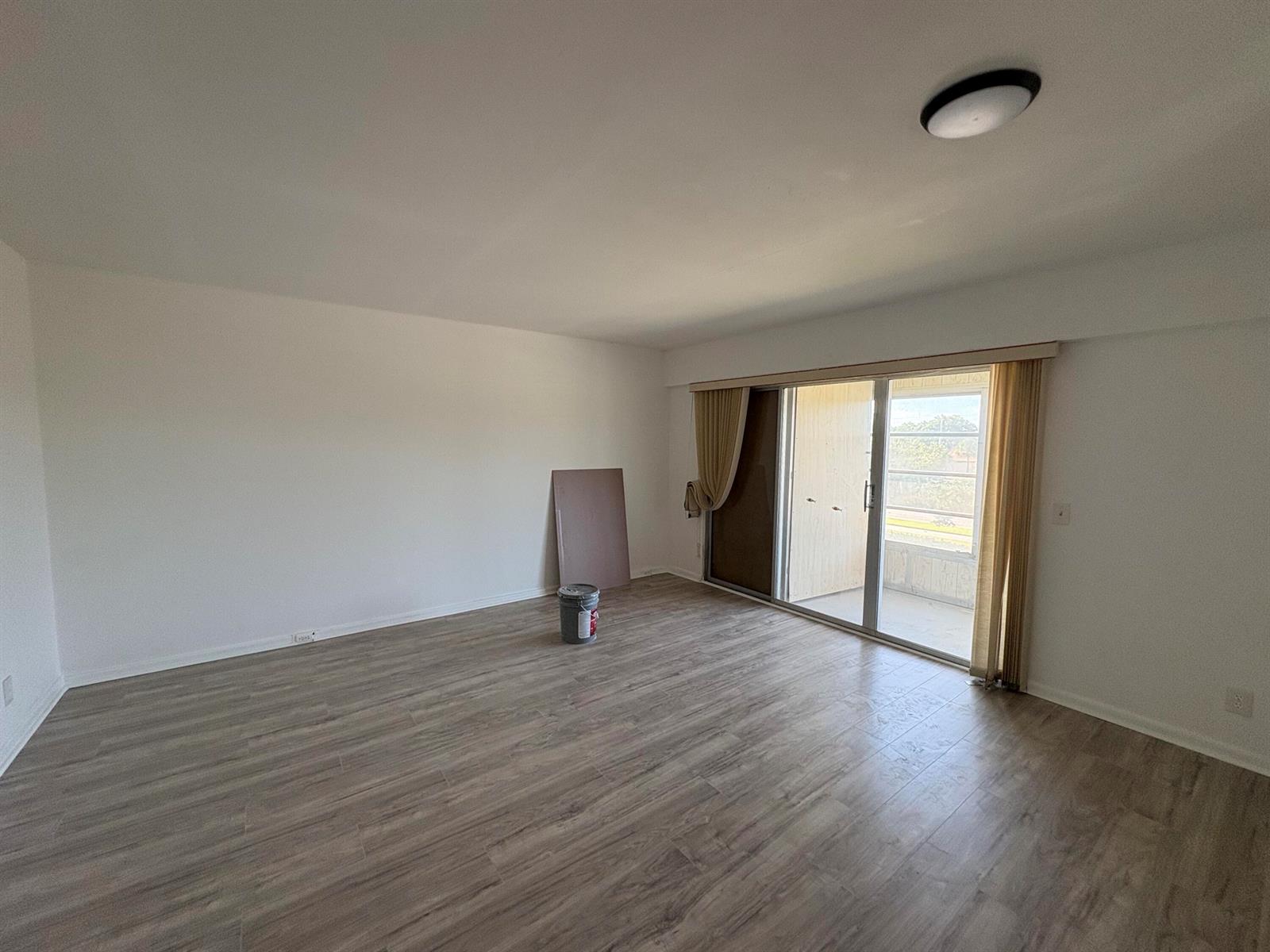 An empty room with wood-look flooring, white walls, and a sliding glass door to a balcony — 497 Mansfield L, Boca Raton FL 33434, BOCA RATON, FL